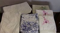 Image of vintage linens showing embroidered pillow cases, Battenberg lace curtain, and blue patterned fabric.