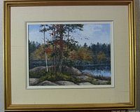 Framed landscape oil painting with autumn trees by a body of water, signed by artist.
