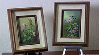 Two framed floral paintings displayed on wall and easel