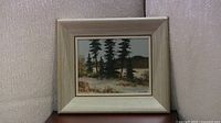 Full view of the framed winter landscape painting showing pine trees and snow with muted background colors.