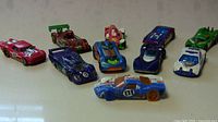 Ten Hot Wheels cars arranged in two rows, various models with colors red, purple, blue, green, and white