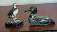 Front view of the puffin standing on a textured rocky base next to the black and white loon lying on display