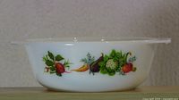 Side profile of the white glass casserole dish showing the colorful vegetable pattern around the body.