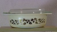 Side view of the Pyrex casserole dish showing the Golden Acorn pattern and clear glass lid.
