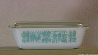 Side view of the rectangular Pyrex refrigerator dish with lid, showing the blue-green Amish Butterprint design on white glass.