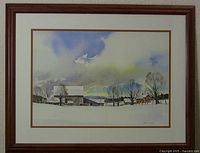 Framed watercolor painting depicting snow-covered farm buildings, houses and trees under a cloudy sky