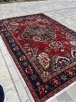 Full view of red Persian Bakhtiari rug displayed outdoors on paved surface