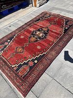 Full view of red Hamadan rug laid on outdoor patio.