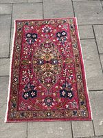 Full top view of the small rectangular handmade rug showing the floral medallion pattern with pink background and brown and blue details.