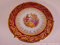Front of antique Limoges porcelain plate with red and gold border and painted romantic scene