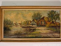 Frontal image of the oil painting showing the winter village scene with houses, trees, a canal, and boats framed in gold.