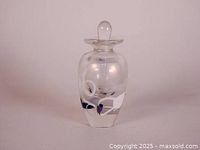 Front view of clear hand blown perfume bottle with white flower and purple details on the front
