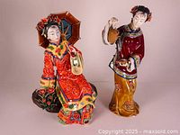 Front view of two Chinese porcelain figurines, one seated with umbrella and one standing pouring tea