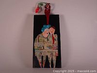 Front view of signed hand-painted Mid-Century Modern artwork on wood showing two figures with collage design and attached red flower.