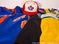 Photo showing assortment of vintage sports jerseys and New Era Blue Jays hat, highlighting colors and logos on jerseys and hat.