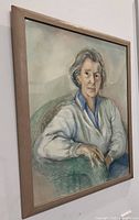 Front view of framed watercolor portrait depicting a woman seated in a green chair, wearing a gray cardigan and blue shirt.
