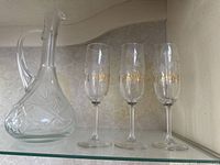 Photo showing three wine glasses and one crystal decanter on a shelf.