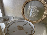Wide view showing three plates: two white ceramic plates with gold accents and one decorative plate with a gold metallic rim and translucent center with lace design.