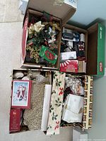 Four opened boxes filled with assorted Christmas decorations including flowers, ornaments, and lights, with some items still in packaging.