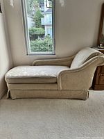 Cream coloured settee sofa showing right side profile with rolled back and right armrest, floral fabric upholstery.