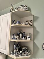 Three-tier shelf with various blue and white Dutch-themed porcelain figurines and decorative items including windmills, characters, cat figurine, a ceramic pitcher, and small containers.