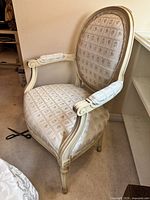 Side angle view of the vintage light-coloured wood armchair showcasing the upholstery and carved wooden frame details.