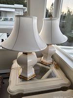 Photo showing the full view of the two matching white ceramic lamps with gold bases and white fabric shades placed on a table.