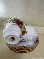 Close-up of a teacup upside down on saucers showing mark on base indicating Royal Albert brand and Old Country Roses pattern.