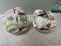 Two stacks of multicolor bone china tea cups and matching saucers with floral and fruit patterns, gold trim visible on handles and rims.