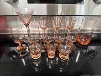 Collection of pink depression glass drinking glasses arranged on stove.