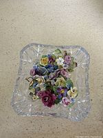 Top view of porcelain floral pins arranged inside a clear cut crystal bowl, showing detail of flower colors and crystal patterns.