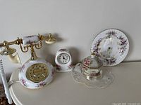 Overall set showing ceramic rotary-style telephone, small matching clock, china dish, trinket box, and Royal Albert decorative clock plate with floral and gold accents.