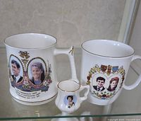 Front view of all three British royalty commemorative cups showing detailed portraits and decorations
