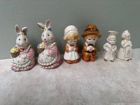 Front view of the set of six ceramic salt and pepper shakers and figurines including two bunny pairs, pilgrim couple, and three small white figurines.