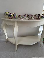 White wooden sofa table showing curved legs, scalloped lower shelf, and smooth finish.