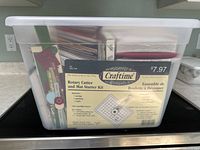 Clear plastic tote containing Craftime rotary cutter kit and other card making craft supplies seen on kitchen counter.