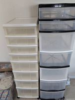 Side-by-side view of two tall plastic storage totes with multiple drawers, one white and translucent, the other black and white with darker trays.