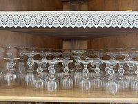 Shelf holding upside-down clear glasses with various stem styles and sizes.