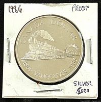 Obverse side of the 1986 silver proof dollar showing a steam locomotive, sun and cityscape, with inscriptions and markings indicating it is silver .5000 and proof condition.