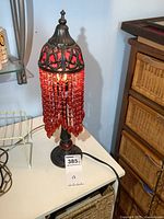 Full view of the metal accent lamp showing 17 inch height, dark metal base and top, and red bead fringe hanging down.