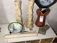 Image showing large resin candle holders, porcelain plate, trinket boxes, porcelain vase, and rolled painting laid out on a surface.