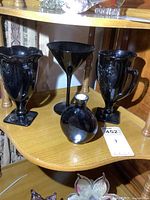 Four pieces of black amethyst glass on a wooden shelf with light reflections, showing different shapes and sizes.