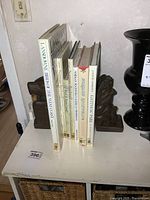 Seven large hardcover books and pair of carved wooden bookends placed on a table.