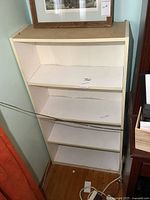 Front view of white melamine bookshelf showing four shelves with minor wear and marks.