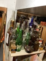 Photo showing a collection of various colored glass bottles including clear, brown, green, and blue bottles on a shelf with an Ansco full tin box