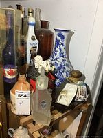 Photo showing grouped bottles and vase on wooden crate, featuring blue-white vase, Dalmatian doghouse bottle, ceramic jug and frosted bottle