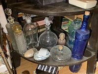 Various glass decanters, bottles, and trinket boxes displayed on a wooden round table shelf.