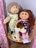 Two vintage Cabbage Patch Kids dolls and plush Odie dog seated on a wooden chair, showing the entire lot.