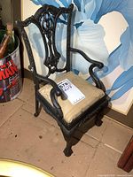 Side view of small doll-sized cast iron chair showing ornate back and arm design with cushioned seat.