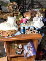 Overview of collectibles including a white furry cat figure in basket, several resin dolls, a decorative tin, and smaller figurines on wooden shelves.